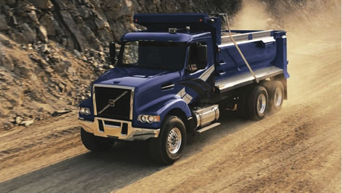 Dump truck driving down dirt road.